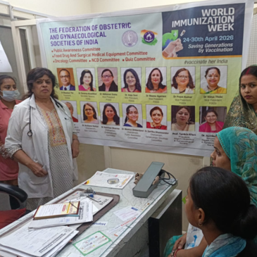 Doctor counseling patients in a hospital consultation room during a World Immunization Week 2026 awareness campaign, with a FOGSI educational banner promoting vaccination and women's health in the background.