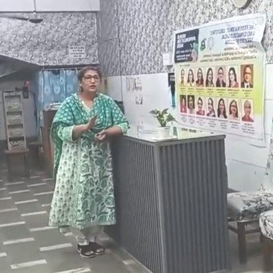 Healthcare professional delivering an awareness session inside a hospital reception area, standing beside an educational poster promoting women's health, medical education, and community healthcare initiatives.