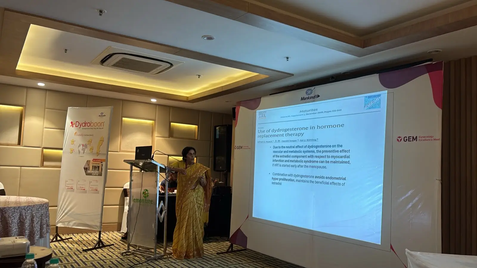 Medical expert delivering a healthcare presentation at a clinical seminar using a projector screen in a professional conference hall.