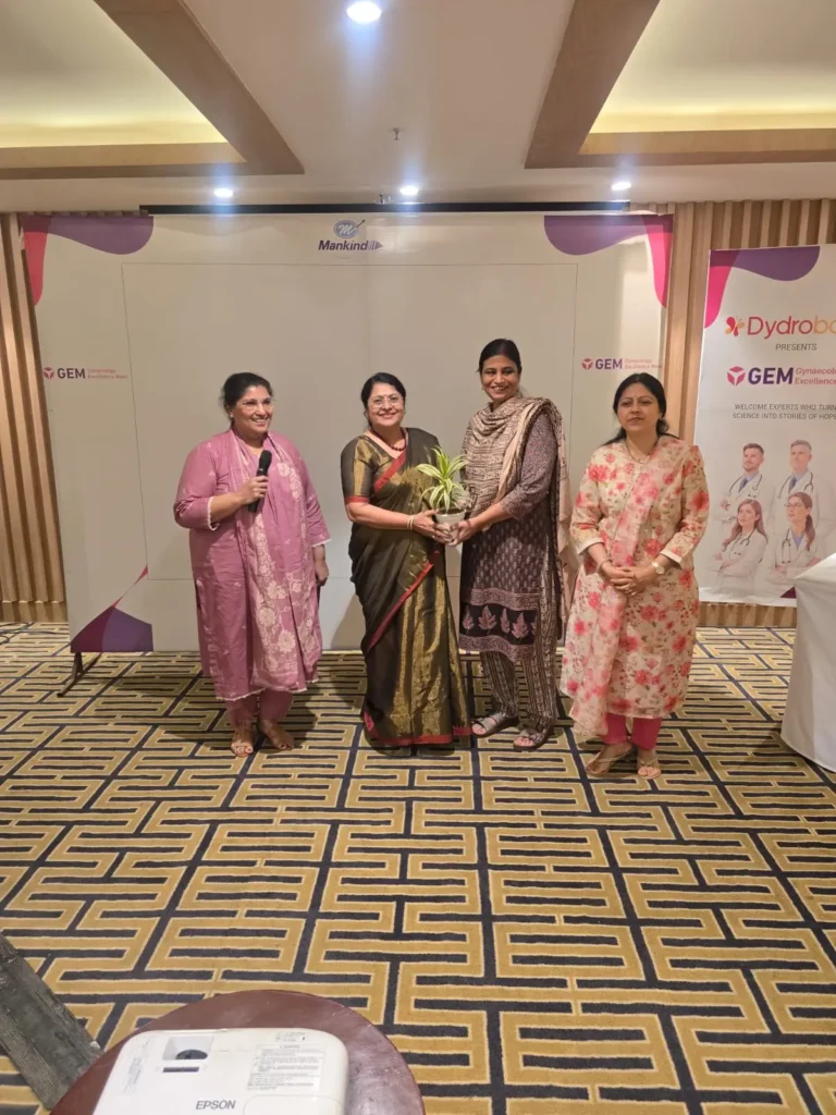 Women being honored with a plant sapling during a healthcare event, standing together on a stage at an indoor conference venue.