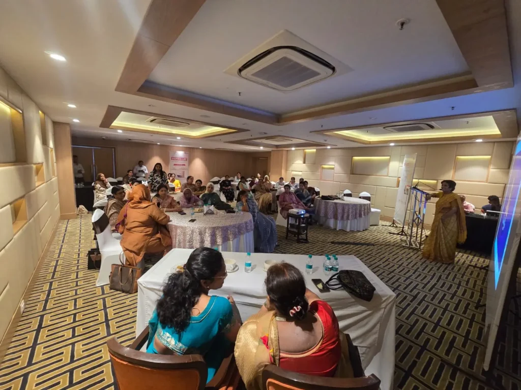 Audience attending a women's health awareness seminar in a conference hall while a speaker delivers an educational healthcare presentation.
